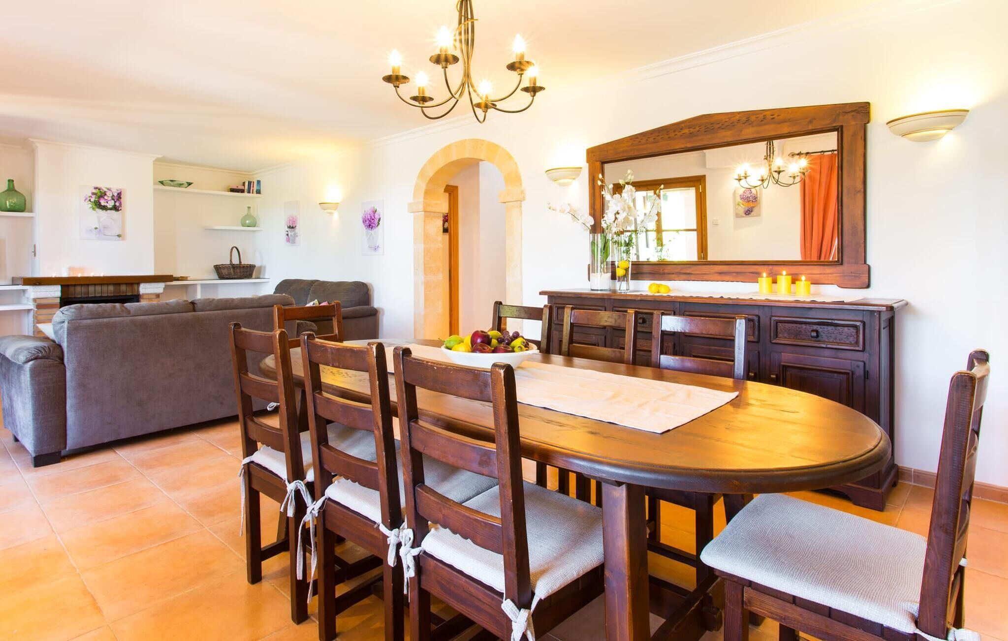 A dining area with a round wooden table, six wooden chairs, and a chandelier.