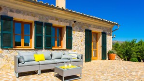 A stone building with green shutters, a gray sofa with cushions, and a glass coffee table with candles. - Gorgeous home in Arta with private swimming pool, can be inside or outside (Arta)