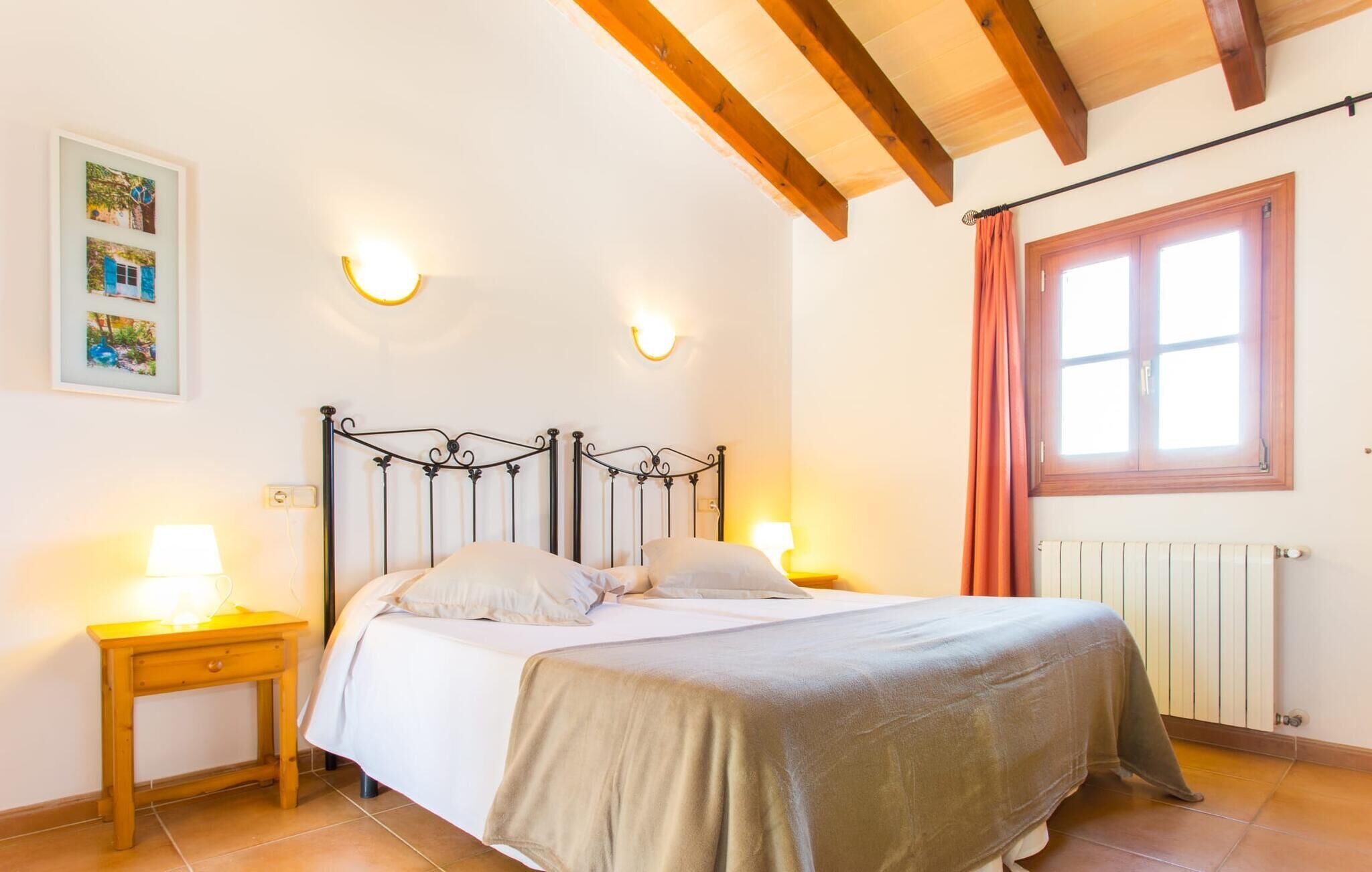 A bedroom with a bed, two bedside lamps, a window with curtains, and a radiator.