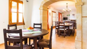 A dining area with a round table and chairs, a bowl of fruit, and a view into the kitchen. - Gorgeous home in Arta with private swimming pool, can be inside or outside (Arta)