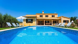 A large swimming pool with lounge chairs and umbrellas, surrounded by a two-story building with a tiled roof and a garden. - Awesome home in Arta with private swimming pool, can be inside or outside (Arta)