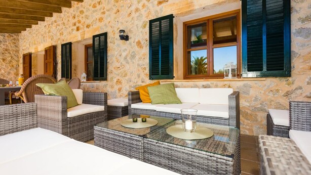 A stone-walled room with wicker furniture, a glass table, and a white sofa with cushions. - Awesome home in Arta with private swimming pool, can be inside or outside (Arta)