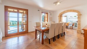 A dining area with a wooden table and chairs, a kitchen in the background, and a view through the open door. - Cozy home in Arta with private swimming pool, can be inside or outside (Arta)