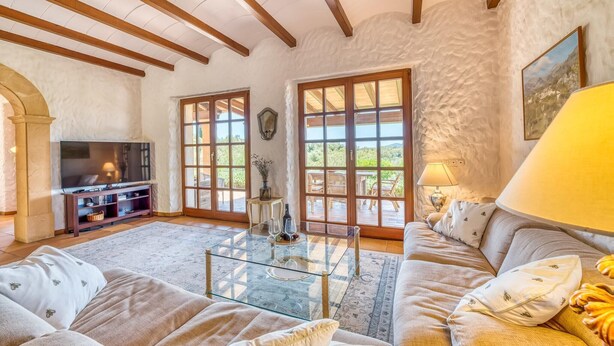 Una sala de estar con televisión, sofá, mesa de centro de vidrio y ventanas amplias.