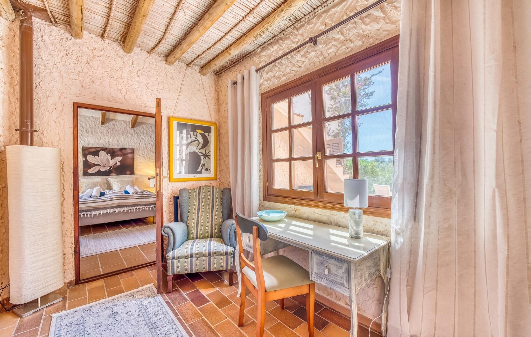 Una habitación acogedora con una cama, un escritorio y una silla. Hay una ventana con cortinas, un cuadro en la pared y una lámpara en el escritorio.