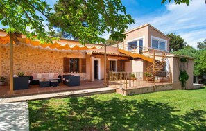 Une maison à deux étages avec une façade en pierre, un patio couvert aménagé avec du mobilier d’extérieur et un escalier menant à l’étage supérieur.