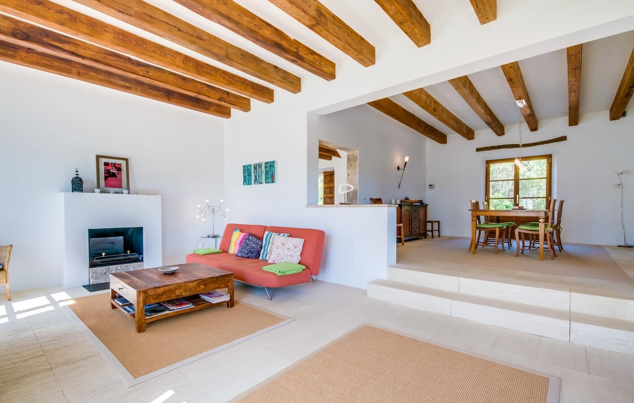 A spacious living room with a fireplace, a red sofa, and a dining area with wooden furniture.