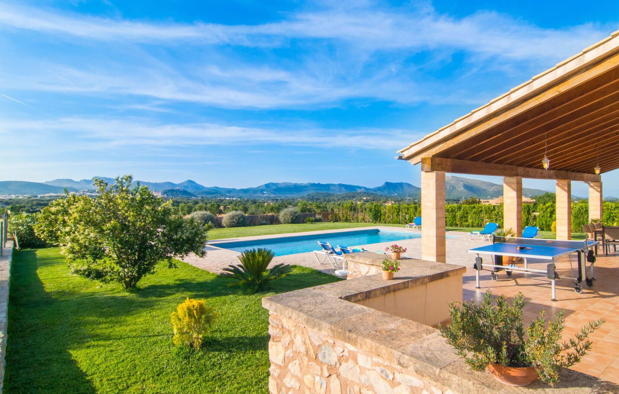 Un espace piscine offrant une vue sur les montagnes, un patio couvert avec des sièges et une pelouse bien entretenue.