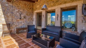 Eine Terrasse mit Steinmauern, Korbmöbeln, einem Glastisch und einer hängenden Leuchte.