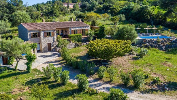 Ein Haus aus Stein mit einem Ziegeldach, umgeben von üppiger Vegetation und einem Swimmingpool.