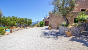 A stone building with a gravel driveway, potted plants, and a view of mountains. - Cozy home in Deia with private swimming pool, can be inside or outside (Deia)