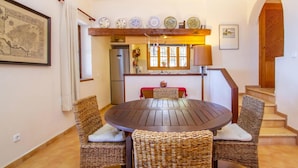 A dining area with a round table and wicker chairs, a kitchen with a refrigerator, and a staircase leading upstairs. - Cozy home in Deia with private swimming pool, can be inside or outside (Deia)