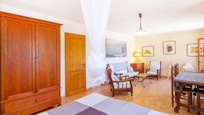 A room with a large wooden wardrobe, a dining table with chairs, a bed with a white canopy, and artwork on the walls. - Cozy home in Deia with private swimming pool, can be inside or outside (Deia)