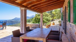 An outdoor patio with a wooden table and wicker chairs, overlooking a scenic landscape with mountains and the sea. - Cozy home in Deia with private swimming pool, can be inside or outside (Deia)