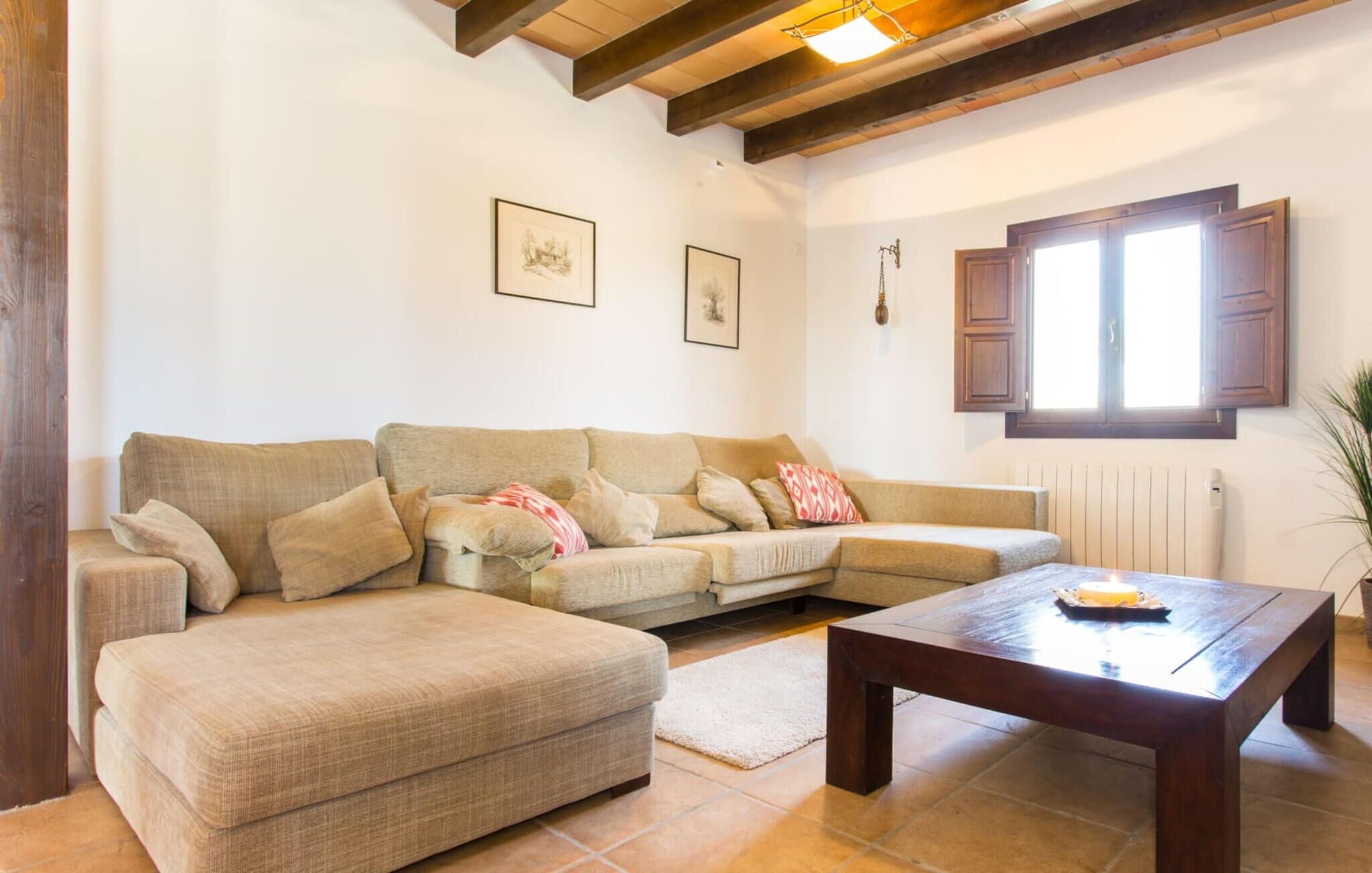 A living room with a beige sectional sofa, a wooden coffee table, and a window with wooden shutters.
