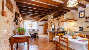 Un coin repas rustique avec des tables et des chaises en bois, un mur en pierre et un sol carrelé.