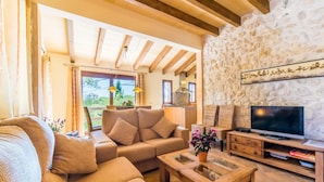 A cozy living room with a stone wall, wooden beams, a sofa set, a coffee table, and a TV. - Stunning home in Santa Margalida (Santa Margalida)
