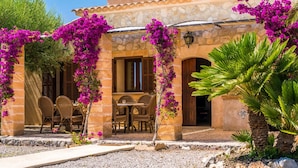 A stone building with a patio area featuring wicker furniture and bougainvillea vines. - Stunning home in Santa Margalida (Santa Margalida)