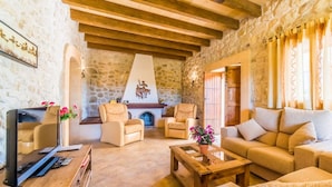 A cozy living room with stone walls, wooden beams, a fireplace, and comfortable seating. - Stunning home in Santa Margalida (Santa Margalida)