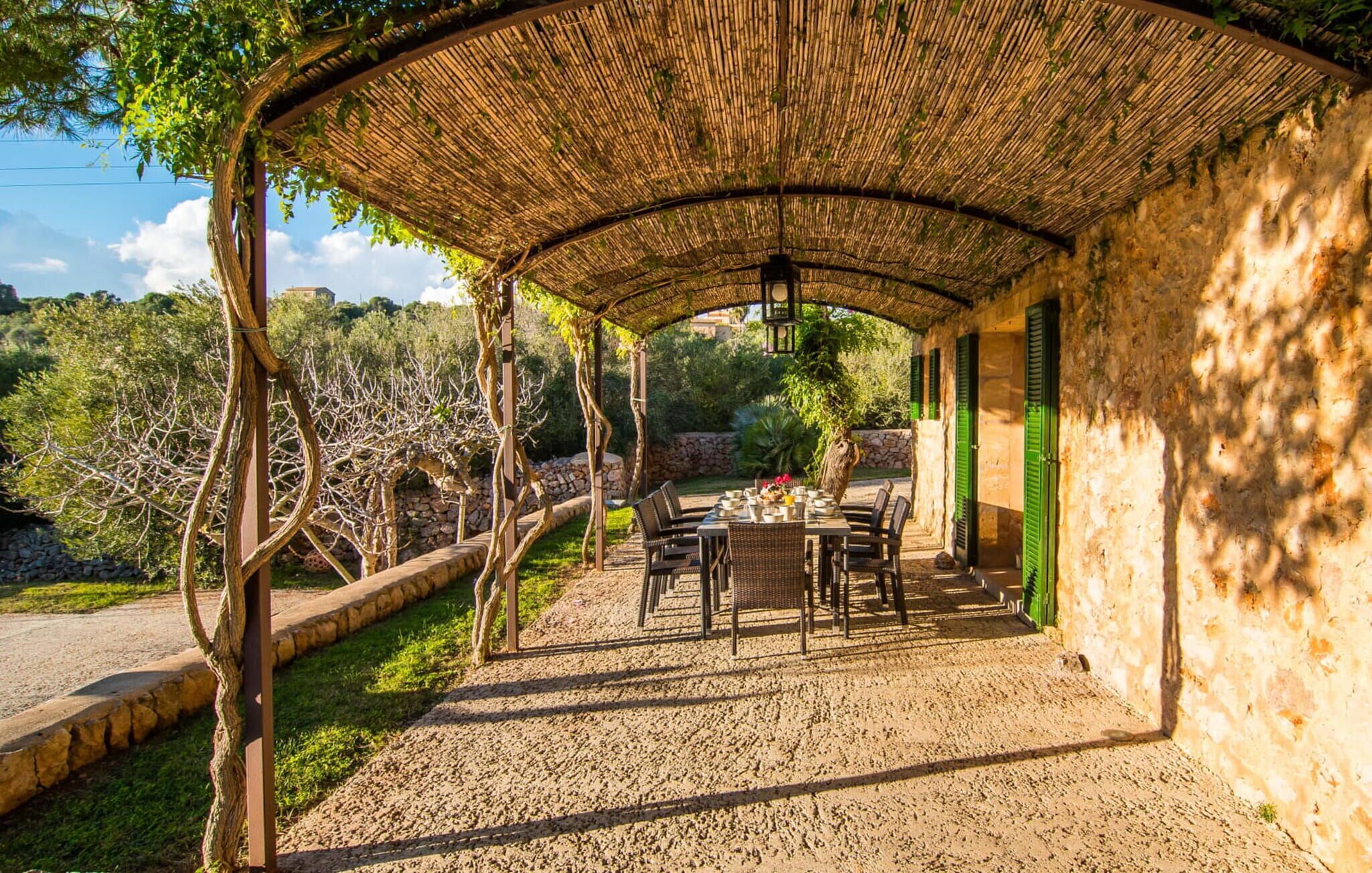 A covered outdoor dining area with a table set for two, surrounded by stone walls and greenery.