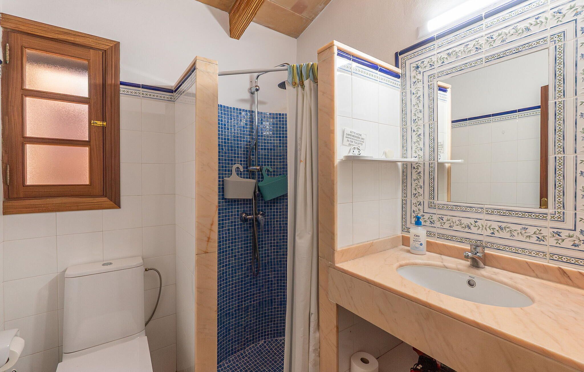 Ein Badezimmer mit Dusche, Toilette, Waschbecken und einem Spiegel mit dekorativem Rahmen.