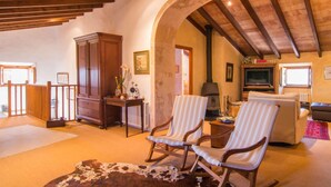 A cozy living room with wooden beams, a large wooden cabinet, two striped armchairs, a sofa, and a television. - Cozy home in Arta with private swimming pool, can be inside or outside (Arta)