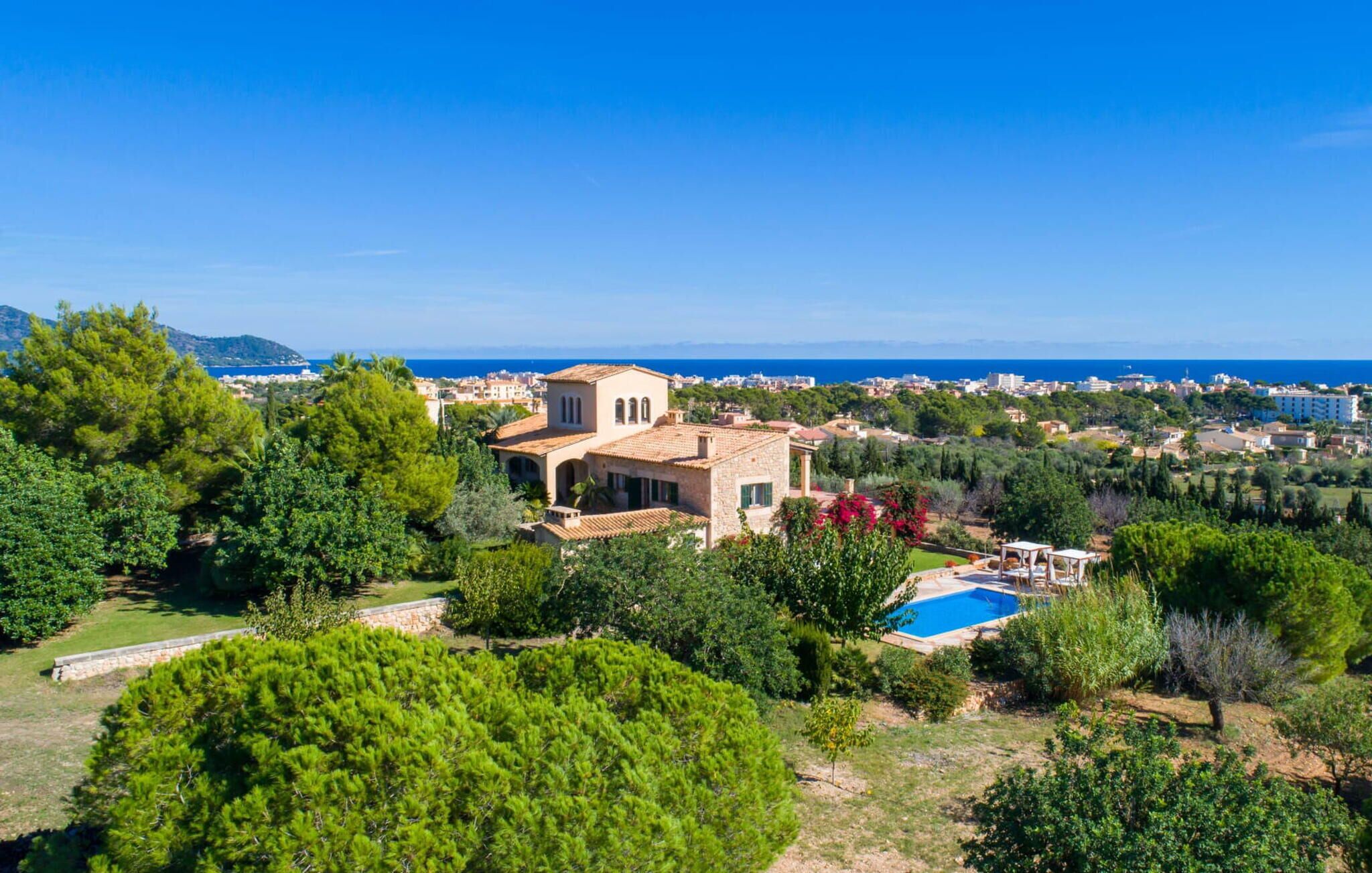 Une villa de style méditerranéen avec piscine, entourée d’une végétation luxuriante et offrant une vue sur une ville côtière.