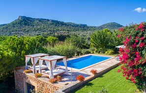 A swimming pool with a stone deck, surrounded by lush greenery and a view of mountains. - Stunning home in Cala Millor (Cala Millor)
