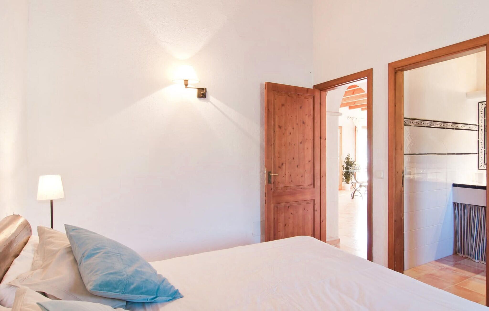Une chambre à coucher comprenant un lit, une table de chevet, une lampe et une porte en bois donnant sur une autre pièce.
