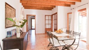 A dining area with a glass table, chairs, and a vase of flowers. There is a wooden ceiling and a door with glass panels. - Luxurious home in Son Servera (Son Servera)