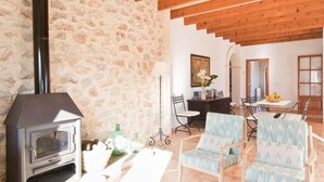 A rustic interior with a stone wall, a wood-beamed ceiling, a fireplace, a dining area with a glass table, and a seating arrangement. - Luxurious home in Son Servera (Son Servera)