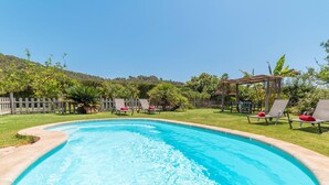 A swimming pool with lounge chairs and a pergola, surrounded by a wooden fence and greenery. - Lovely home in Son Servera with private swimming pool, can be inside or outside (Son Servera)