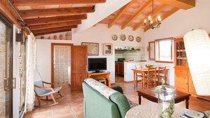 A cozy living room with a television, sofa, and dining table. There is a kitchen in the background with a window and a chandelier. - Lovely home in Son Servera with private swimming pool, can be inside or outside (Son Servera)