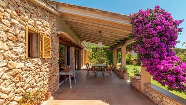 A stone building with a covered patio, a table with chairs, and vibrant purple bougainvillea flowers. - Lovely home in Son Servera with private swimming pool, can be inside or outside (Son Servera)