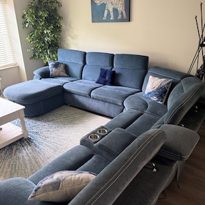 Een modulaire bank met chaise longue, een bijzettafeltje en een plant in een woonkamer.
