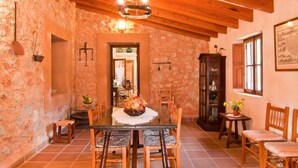 Un comedor rústico con pared de piedra, vigas de madera en el techo y una araña.