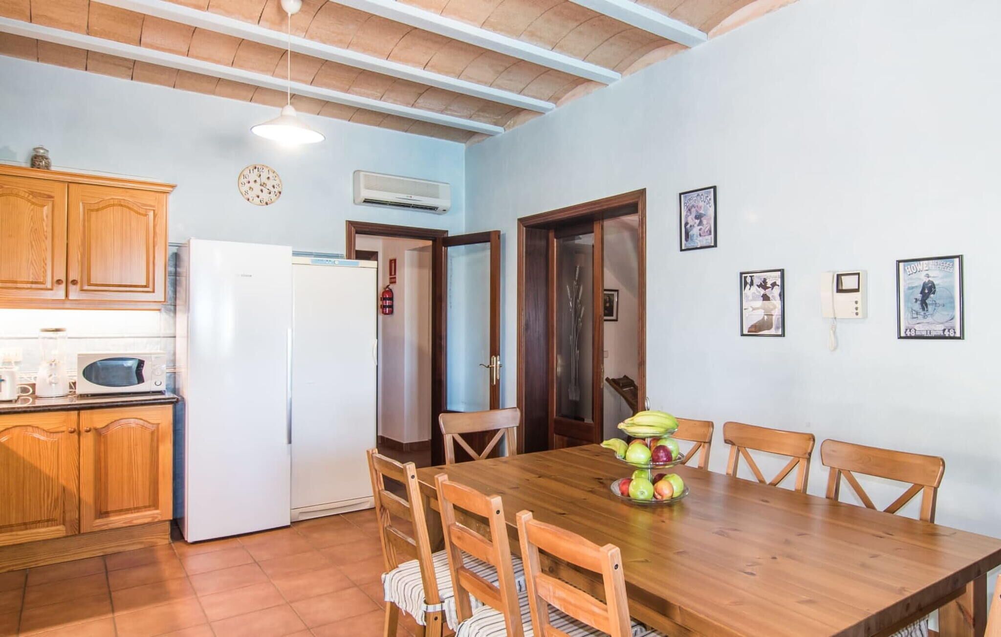 A dining area with a wooden table and chairs, a kitchen with wooden cabinets and a white refrigerator, and a ceiling with exposed beams.