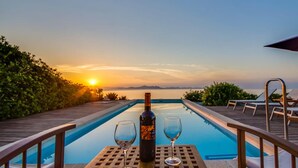 Une vue sur la piscine au coucher du soleil, une bouteille de vin et deux verres sur une table.