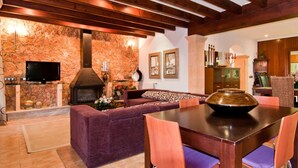 Un accogliente soggiorno con parete in pietra, camino, divano, tavolo da pranzo e TV.