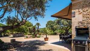 Eine Außenpatio-Terrasse mit Steinmauer, Grill und mehreren Tischen und Stühlen.