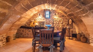 Un espace de restauration souterrain avec des murs en pierre, une table ronde, des chaises en bois et un lustre.