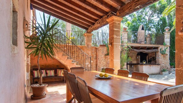 Une table à manger en bois, des chaises, une plante en pot et un escalier menant à un balcon.