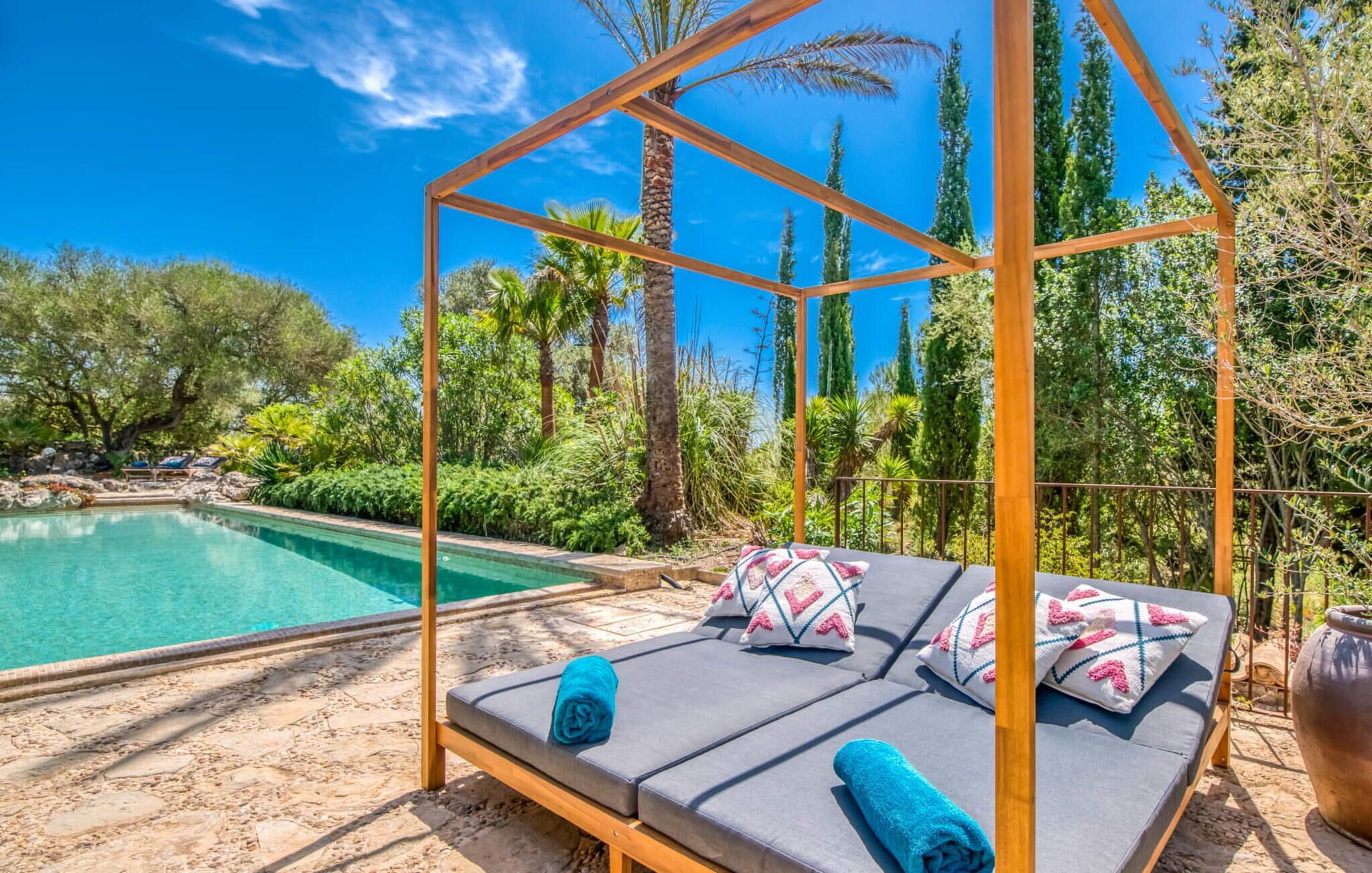 A wooden canopy with a cushioned bench, a pool, and lush greenery.