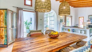 Ein geräumiges Wohnzimmer mit einem Holzesstisch, Korbstühlen und einem großen Fenster, das für natürliches Licht sorgt.