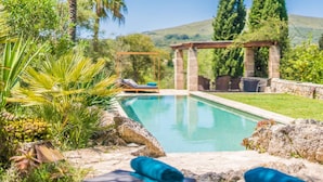 Ein Poolbereich mit Pergola, Liegestühlen und einem Kiesweg.