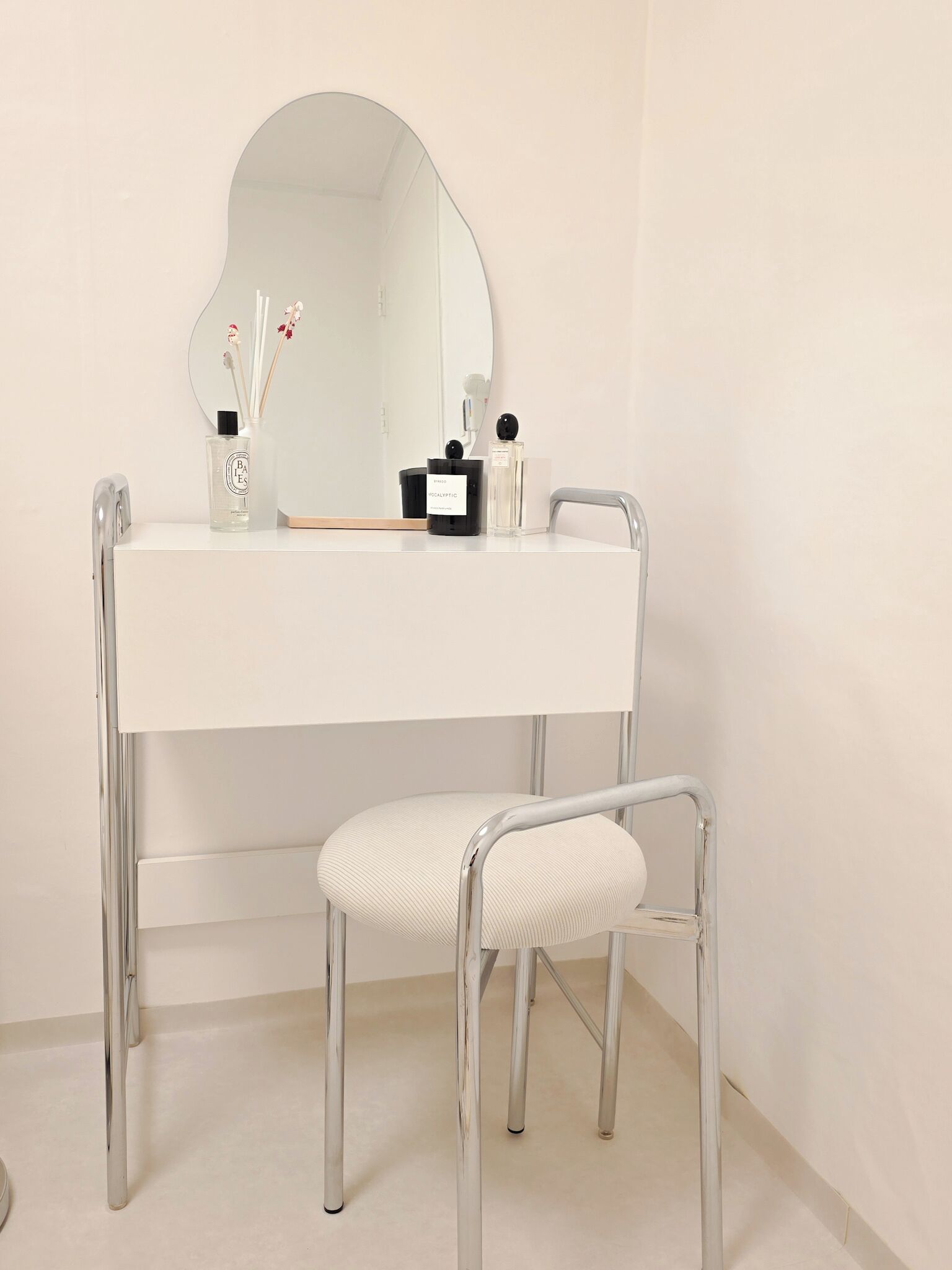 A white vanity with a round mirror, a small table, and a chair.