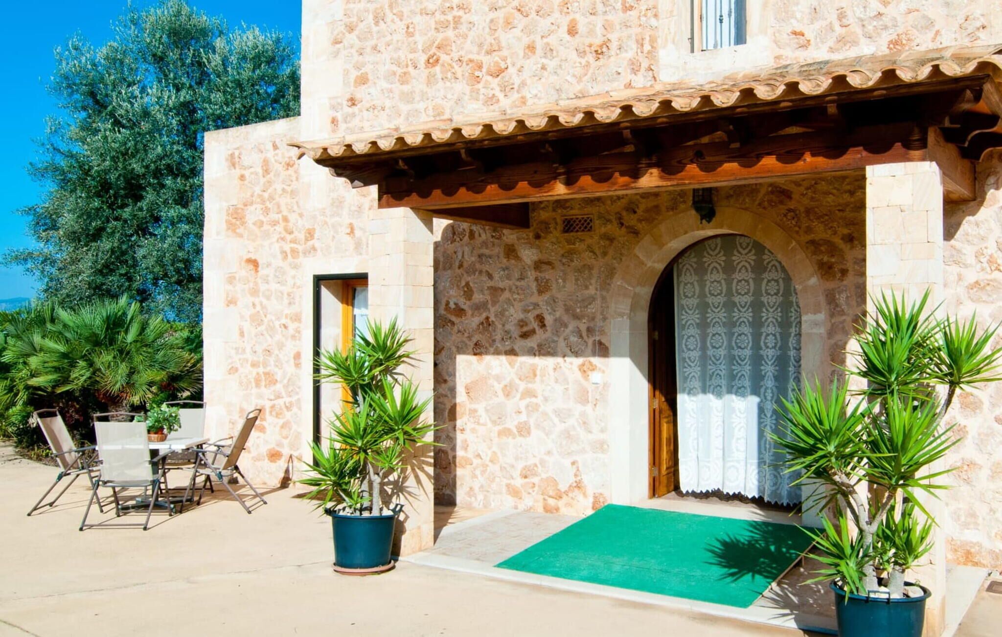 A stone building with a tiled roof, a green mat at the entrance, and potted plants.