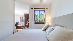 Ein Schlafzimmer mit einem großen Bett, einem Nachttisch mit Lampe, einer Kommode und einem Fenster mit Vorhängen.