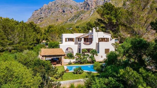 Eine weiße Villa mit Pool, umgeben von Grün und Bergen.