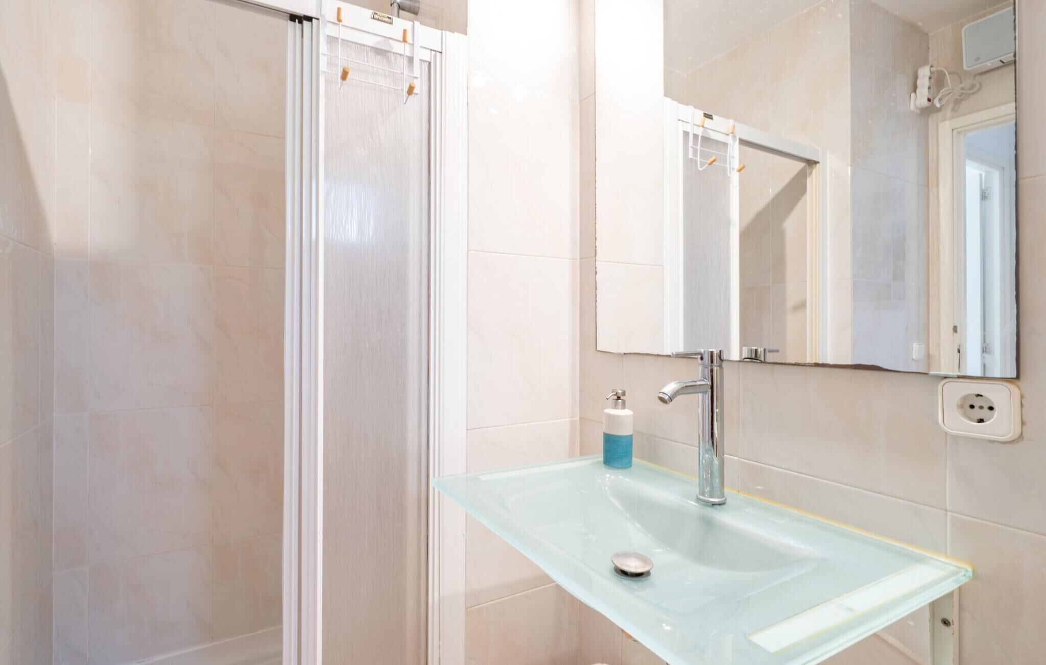 Une salle de bain avec un lavabo en verre, un miroir et un espace douche.